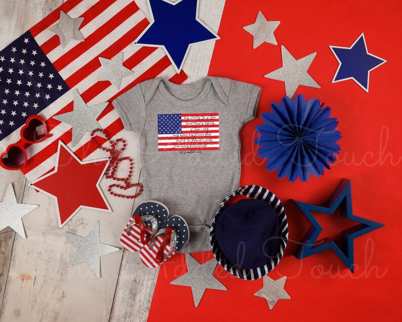 May include: A gray baby onesie with a red, white, and blue American flag and text on the front. The onesie is surrounded by red, white, and blue stars, a blue fan, and red and white heart-shaped sunglasses.