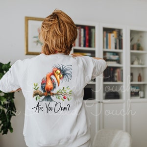 Pode incluir: Camisola branca com uma ilustra&ccedil;&atilde;o de um p&aacute;ssaro de desenho animado e o texto "Are You Okay?" impresso nas costas.