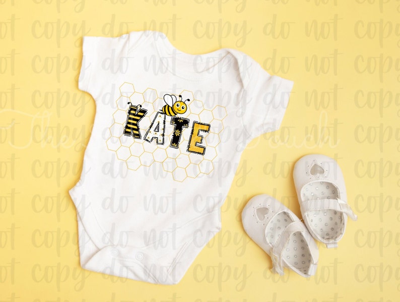 May include: White baby onesie with a bee and honeycomb design. The onesie has the name "KATE" spelled out in yellow and black letters. Two white baby shoes are on a yellow background.