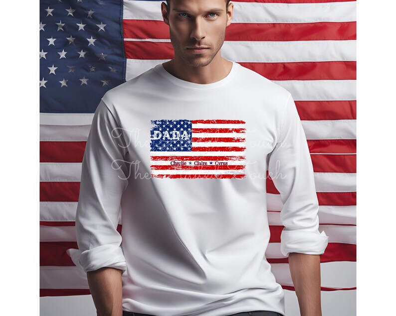 May include: White long-sleeve shirt with a distressed American flag design. The flag has the word "DADA" in blue lettering and the names "Charlie", "Claire", and "Cruz" in smaller blue lettering below the flag.