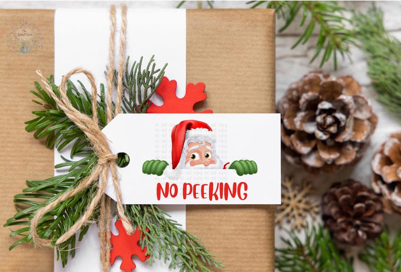 May include: A wrapped gift with a white tag featuring Santa Claus peeking over the top. The tag reads "NO PEEKING" in red letters. The gift is decorated with greenery, twine, and red snowflake accents.
