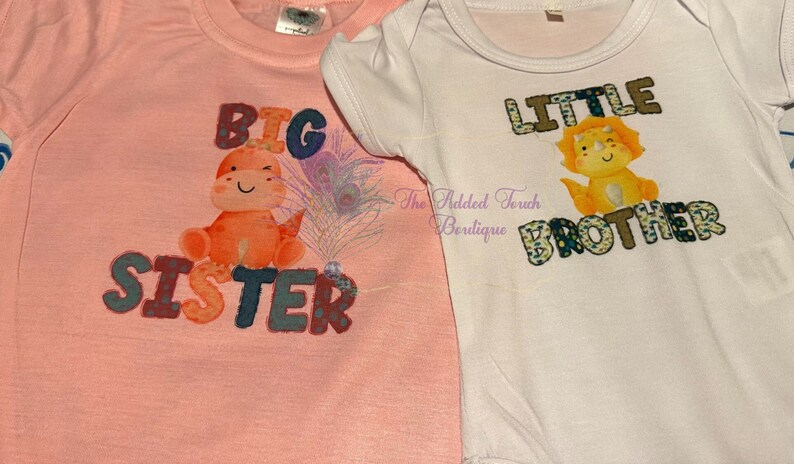 K&ouml;nnte beinhalten: Zwei rosa und wei&szlig;e T-Shirts mit Dinosaurier-Grafiken. Das rosa Shirt sagt "Gro&szlig;e Schwester" und das wei&szlig;e Shirt sagt "Kleiner Bruder".