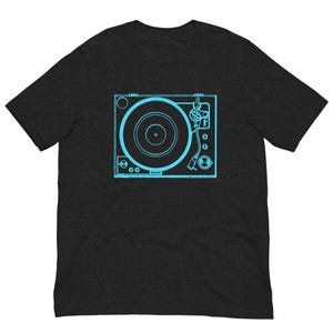 Puede incluir: Camiseta gris oscuro con un contorno azul claro de un tocadiscos. El diseño muestra el disco, el brazo fonocaptor y el panel de control. La camiseta está hecha de un material suave.