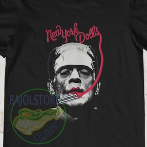 May include: Black t-shirt with a graphic of Frankenstein wearing lipstick and a microphone with the text "New York Dolls" above him.