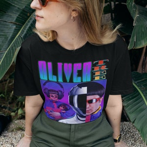 May include: Black t-shirt featuring a graphic print of a band called "Oliver Tree". The graphic depicts a person wearing a helmet and sunglasses, and another person wearing headphones and sunglasses.