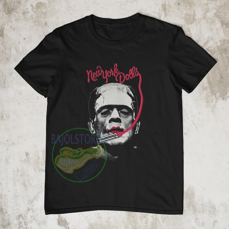 May include: Black t-shirt with a graphic of Frankenstein wearing lipstick and a microphone with the text "New York Dolls" above him.