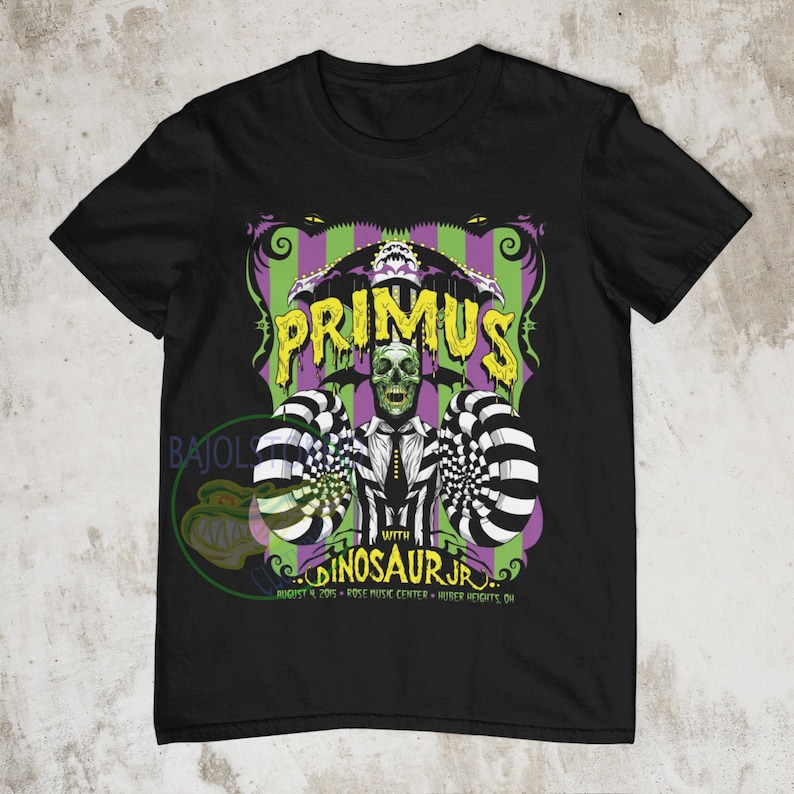 May include: Black t-shirt with a graphic of a skull wearing a suit and a top hat. The graphic is in front of a striped background with the text "PRIMUS" and "WITH DINOSAUR JR." The text below the graphic reads "AUGUST 4, 2015 - ROSE MUSIC CENTER - HUBER HEIGHTS, OH."