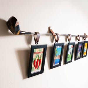Peut inclure: Pr&eacute;sentoir photo mural original avec une t&ecirc;te de club de golf vintage. La tige m&eacute;tallique avec des boucles en cuir supporte des tirages encadr&eacute;s en noir. Les tirages pr&eacute;sentent des affiches de voyage color&eacute;es.
