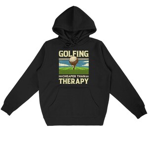 May include: Black hoodie with a white graphic that says "Golfing - Cheaper Than Therapy" with a golf ball on a green golf course.