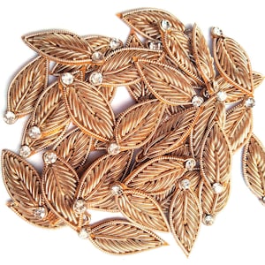 May include: A pile of gold leaf embellishments with clear rhinestones. The embellishments are shaped like leaves and are perfect for adding a touch of sparkle to any craft project.