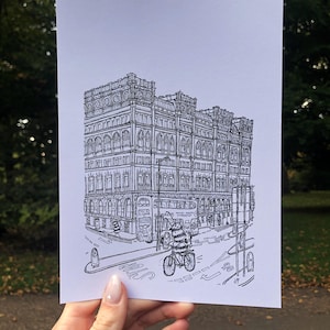 May include: Black and white line drawing of a large building with a bus and a person riding a bicycle in front of it. The building has many windows and a sign that says "Travel Agents" above the entrance. The person on the bicycle is wearing a helmet and carrying a backpack.