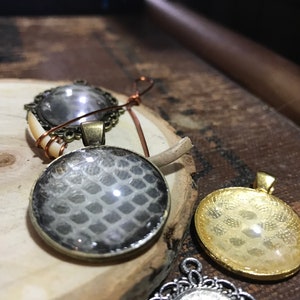 以下が含まれることがあります： 異なるデザインの丸いガラス製のペンダントが3つあります。最初のペンダントは、透明なガラスに銀色のフレームと装飾的なデザインが施されています。2番目のペンダントは、透明なガラスに銀色のフレームとヘビの皮のデザインが施されています。3番目のペンダントは、透明なガラスに金色のフレームと花柄のデザインが施されています。