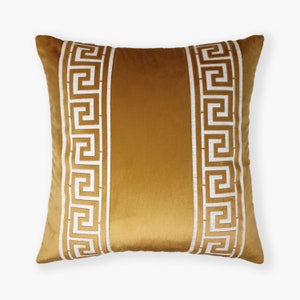 May include: A gold velvet throw pillow with white Greek key pattern trim.