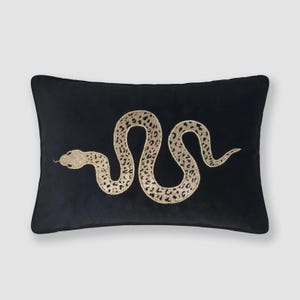 Può includere: Un cuscino rettangolare nero con una grafica di serpente color oro centrata e orizzontale. Il serpente è raffigurato in una posa sinuosa a forma di S ed è riempito con un dettagliato motivo a macchie di leopardo scure su tutto il corpo.