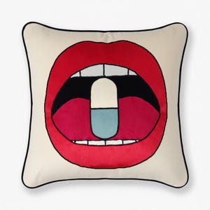 Puede incluir: Cojín cuadrado decorativo con fondo crema y un gráfico audaz de labios rojos con una pastilla blanca en su interior. Los labios están delineados en negro y el cojín tiene un borde negro.