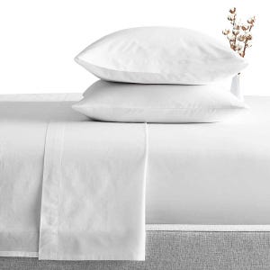 May include: A pristine white bed linen set featuring two stacked pillows. The sheets are neatly arranged on a bed, with a folded top sheet. A small vase with cotton stems is in the background. The bedding has a clean, minimalist design.