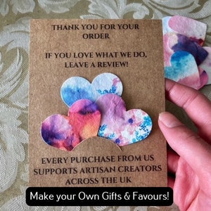 May include: A brown card with the text "Thank you for your order. If you love what we do, leave a review!" and "Every purchase from us supports artisan creators across the UK. Make your own gifts & favours!"  The card has five colourful paper hearts attached to it.