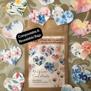 May include: A pack of wildflower seed hearts, made from cotton. The pack is brown with a white label that says "Wildflower Seed Hearts" and "55mm Hearts Handmade from cotton". The pack is surrounded by 10 heart-shaped seed paper, each with a different floral design.