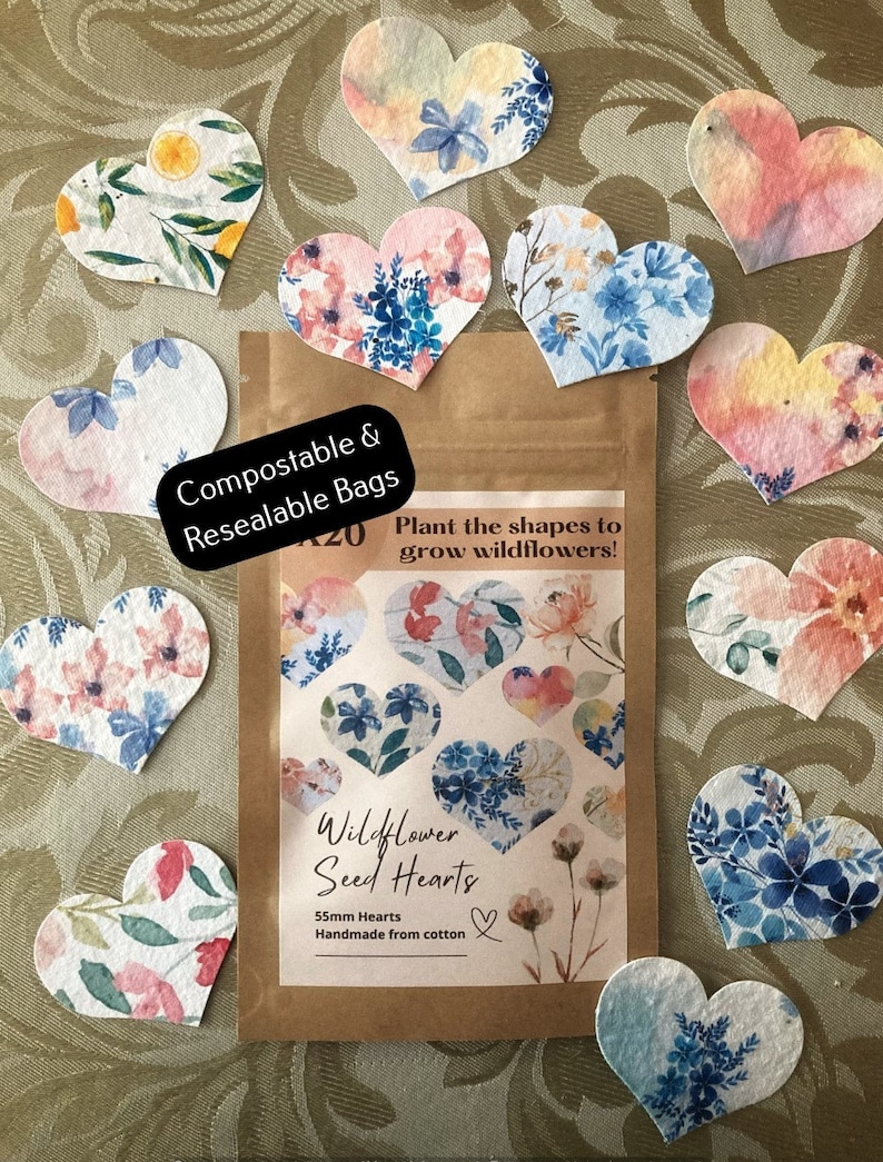 May include: A pack of wildflower seed hearts, made from cotton. The pack is brown with a white label that says "Wildflower Seed Hearts" and "55mm Hearts Handmade from cotton". The pack is surrounded by 10 heart-shaped seed paper, each with a different floral design.
