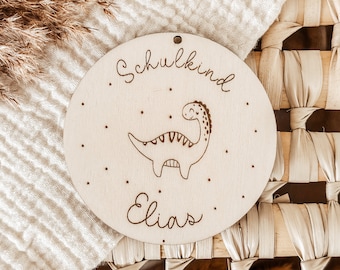 May include: A round wooden sign with a dinosaur illustration and the text "Schulkind Elias".