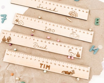 May include: Four wooden rulers with different designs and names: Sarah, Leo, David, and Tim. Each ruler is 20 centimetres long and features a different design, including a rainbow, a tractor, a dinosaur, and a car.