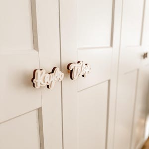 Op de afbeelding: Twee witte houten knoppen voor kastdeuren met de namen "Kayla" en "Taylor" in cursief.