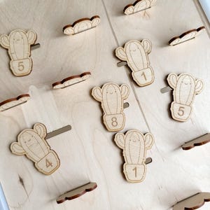 Può includere: Pezzi di puzzle in legno a forma di cactus con i numeri 1, 4, 5 e 8 su uno sfondo in legno chiaro. I pezzi sono disposti in uno schema, con alcuni pezzi sovrapposti.