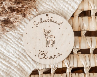 May include: A round wooden sign with the text "Schulkind" and the name "Chiara" written in cursive. A small deer illustration is in the center of the sign.