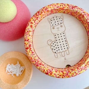 Può includere: Un vaso rotondo, macchiato, rosso e giallo con un inserto in legno che presenta un'illustrazione in bianco e nero di un alpaca. L'inserto in legno ha il testo "SMALL'S CREATIONS".