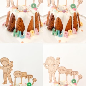 Könnte beinhalten: Ein Gugelhupf mit weißem Zuckerguss und bunten Streuseln, verziert mit Holzausschnitten von Kindern, Sprechblasen mit "HURRA" und "ABC" und anderen Formen. Das Wort "HURRA" ist auch in bunten Buchstaben am Boden des Kuchens geschrieben.