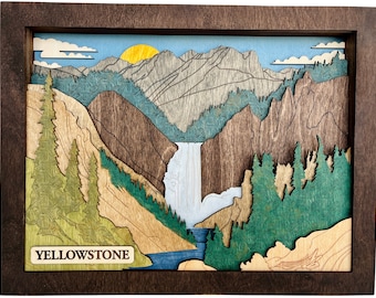 Puede incluir: Una obra de arte de madera en capas que representa un paisaje del Parque Nacional de Yellowstone. La obra presenta una cascada, montañas, árboles y un sol poniente, todo dentro de un marco de madera marrón oscuro. La palabra "YELLOWSTONE" se muestra en la parte inferior.