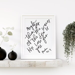 May include: A white framed print with black calligraphy that reads "Mightier than the waves of the sea is His love for you." The text is followed by "Psalm 93:4".