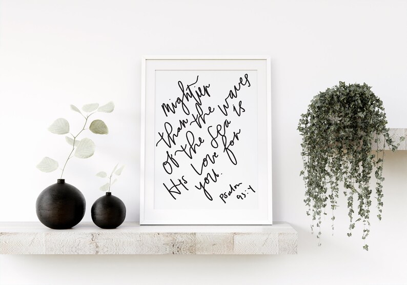 May include: A white framed print with black calligraphy that reads "Mightier than the waves of the sea is His love for you." The text is followed by "Psalm 93:4".