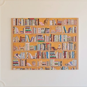 May include: A white wall with ornate molding and a framed print of a bookshelf filled with colorful books. The bookshelf is on a yellow background.