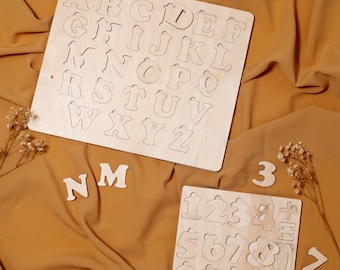 May include: Two wooden puzzles, one with the alphabet and the other with numbers, on a brown fabric background. The alphabet puzzle has the letters A through Z, and the number puzzle has the numbers 1 through 10, plus symbols like plus, minus, equals, and percent.