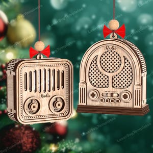 Op de afbeelding: Twee lasergesneden houten ornamenten in de vorm van vintage radio's. Elk ornament heeft een lichte houtafwerking, een rode strik en een kleine houten kraal aan de bovenkant. De vierkante radio heeft de tekst Radio, Vol en FM. De boogvormige radio heeft de tekst Radio.