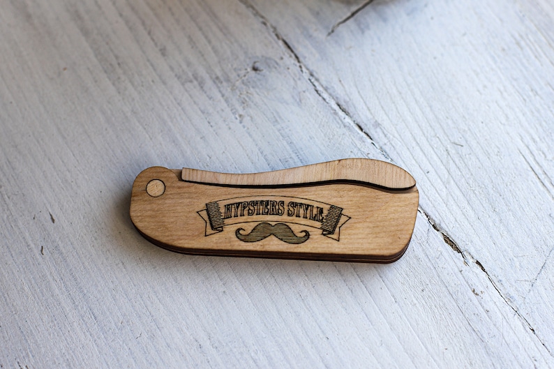 Op de afbeelding: Een houten kam met een gebogen handvat en de tekst "Hipsters Style" met een snor-afbeelding.