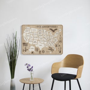 May include: A wooden map of the United States with each state outlined and labeled. The map is mounted on a light brown wall with a chair in front of it. The map has the words "Our Adventures" at the top.