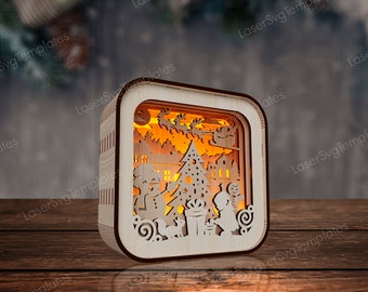 May include: A wooden Christmas-themed lantern with a warm, glowing interior. The design features a snowman, Christmas tree, and Santa's sleigh. The lantern is square with a light brown frame and intricate cut-out details.