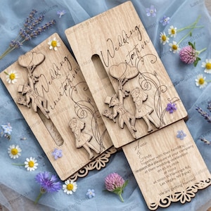 May include: Wooden wedding invitation with laser-cut design. Features a couple with balloons and floral accents. The invitation includes the text "Wedding Invitation" and wedding details. Decorative floral elements surround the invitation.