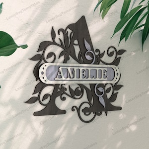 Può includere: Una lettera decorativa in legno A con intricati disegni floreali e una targhetta argentata con la scritta "AMELIE".