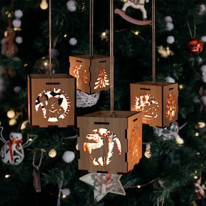 Puede incluir: Cuatro adornos navideños de madera con diferentes diseños, que incluyen un reno, un muñeco de nieve, un árbol de Navidad y un Papá Noel. Los adornos están colgados de un árbol de Navidad y están iluminados desde adentro.