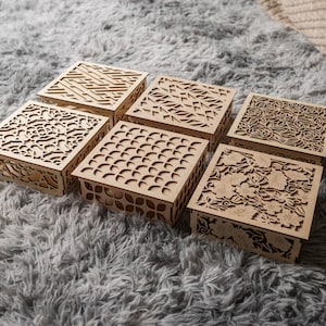 May include: Six wooden boxes with intricate laser cut designs. The boxes are arranged in two rows of three, with the designs featuring geometric patterns, flowers, and abstract shapes.