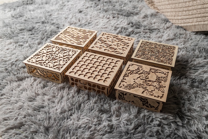 May include: Six wooden boxes with intricate laser cut designs. The boxes are arranged in two rows of three, with the designs featuring geometric patterns, flowers, and abstract shapes.