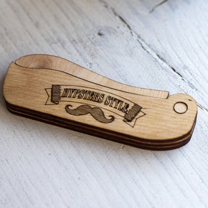 Op de afbeelding: Een houten kam met een snor en de tekst "Hipsters Style" erop gegraveerd.