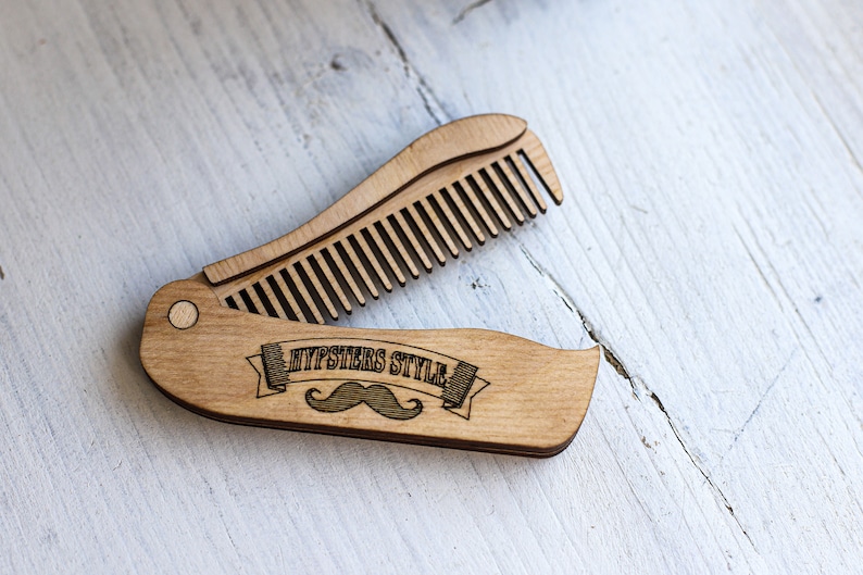 Op de afbeelding: Een houten vouwkam met een snor en de tekst "Hipsters Style" gegraveerd op het handvat.