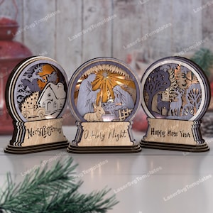 May include: Three wooden Christmas decorations with intricate laser cut designs. The decorations feature a nativity scene, a winter forest, and a Christmas truck. Each decoration has a light inside and a base with a festive message: "Merry Christmas", "O Holy Night", and "Happy New Year".