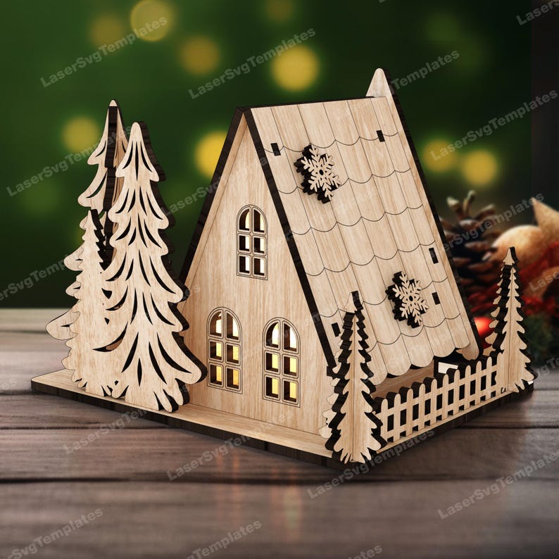 May include: A wooden Christmas house with a triangular roof, two windows, and a small fence. The house is decorated with snowflakes and has a light inside. There are two pine trees on either side of the house.