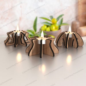 May include: Three wooden candle holders with a star, flower, and geometric design. Each holder has a black center and is designed to hold a tea light candle.