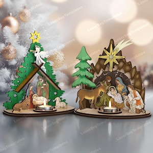 May include: Two wooden Christmas nativity scene candle holders. One is a green tree with an angel and star, the other is a brown cave with a star and figures. Each has a candle holder.